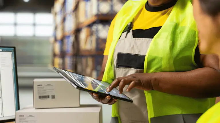 woman holds tablet and talks to coworker with shipping boxes in warehouse